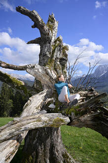 Entspannte Frau sitzt auf einem toten Baum an einem sonnigen Tag - ECPF00950