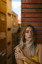 Beautiful woman with long blond hair standing against brick wall in balcony - TCEF00718