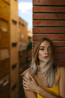 Schöne Frau mit langen blonden Haaren, die auf einem Balkon an einer Ziegelmauer steht - TCEF00718