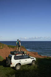 Mid adult couple standing on 4x4 roof while looking at sea against blue sky - VEGF02320