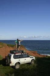 Paar, das auf dem Dach eines 4x4 steht und auf das Meer vor blauem Himmel blickt - VEGF02321