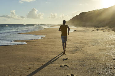 Mann joggt bei Sonnenuntergang auf Sand am Strand - VEGF02323