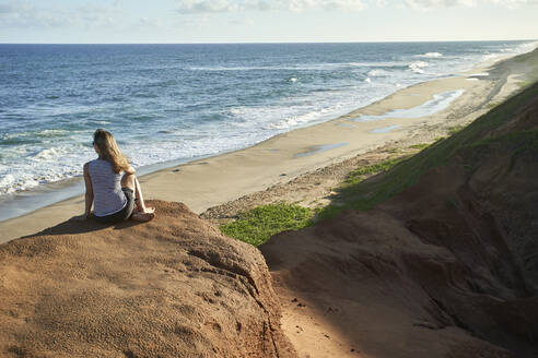 Woman sitting on rock formation while looking at sea - VEGF02324