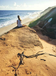 Woman sitting on rock formation while looking at sea during sunny day - VEGF02326