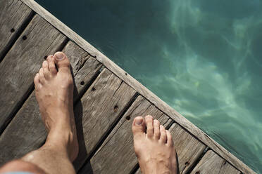 Füße eines Mannes auf dem Boden am Schwimmbad während eines sonnigen Tages - VEGF02331