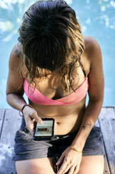 Frau im Bikini surft durch ihr Smartphone - VEGF02333