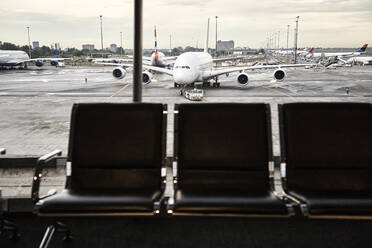 Südafrika, Johannesburg, Flugzeug auf dem Rollfeld vom Flughafenterminal aus gesehen mit leeren Stühlen im Vordergrund - VEGF02336