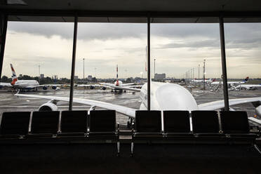 Südafrika, Johannesburg, Flugzeuge auf dem Rollfeld vom Flughafen-Terminal aus gesehen mit leeren Stühlen im Vordergrund - VEGF02339