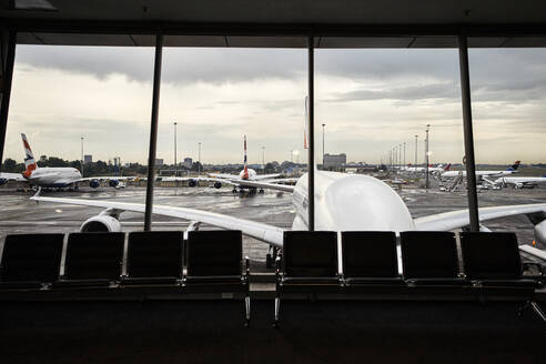 Südafrika, Johannesburg, Flugzeuge auf dem Rollfeld vom Flughafen-Terminal aus gesehen mit leeren Stühlen im Vordergrund - VEGF02339