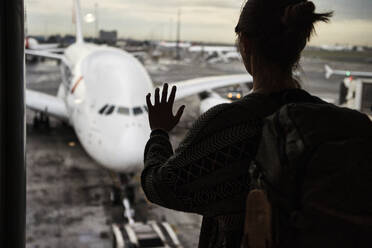 Südafrika, Johannesburg, Rückansicht einer Frau, die vom Flughafenterminal aus ein Flugzeug auf dem Rollfeld betrachtet - VEGF02341