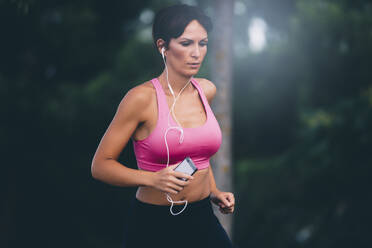 Fit woman listening music while jogging at park - OCMF01313