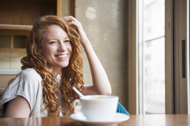 Glückliche Frau sitzt am Tisch mit Kaffeetasse zu Hause - DIGF12465