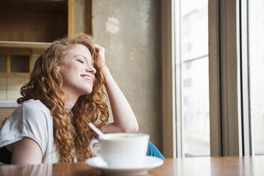 Happy young woman with hand in hair sitting at home - DIGF12466