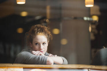 Thoughtful young woman leaning on table seen through glass window in coffee shop - DIGF12470