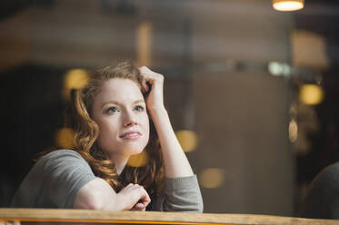 Thoughtful woman leaning on table seen through glass window in coffee shop - DIGF12471