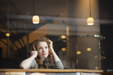 Nachdenkliche Frau, die sich auf einen Tisch stützt, gesehen durch das Fenster eines Cafés - DIGF12472