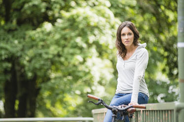 Schöne junge Frau sitzt mit dem Fahrrad auf dem Geländer im Park - DIGF12478