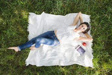 Entspannte junge Frau auf einer Picknickdecke im Park liegend - DIGF12480