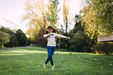 Glückliches Mädchen hört Musik und tanzt auf einer Wiese im Park im Herbst - DCRF00194