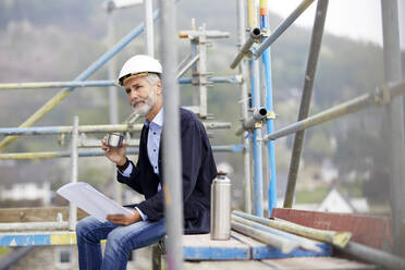 Architekt macht Pause auf einem Baugerüst auf einer Baustelle - MJFKF00210