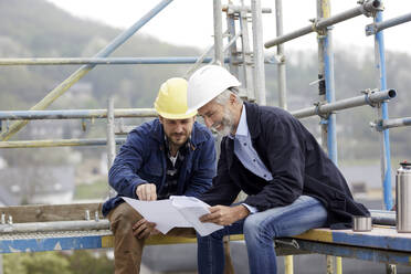 Architekt und Arbeiter besprechen einen Bauplan auf einem Baugerüst auf einer Baustelle - MJFKF00211