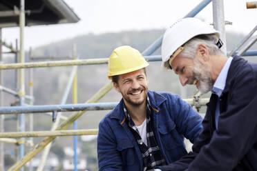 Glücklicher Architekt und Arbeiter auf einem Baugerüst auf einer Baustelle - MJFKF00213