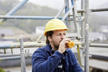 Arbeiter trinkt Saft auf einem Baugerüst auf einer Baustelle - MJFKF00215