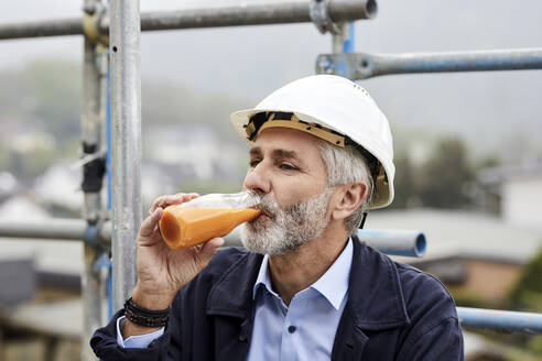 Architekt trinkt Saft auf einem Baugerüst auf einer Baustelle - MJFKF00216