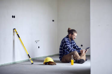 Worker on a construction site sitting on the floor using tablet - MJFKF00232