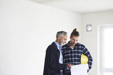 Architect and worker discussing building plan on a construction site - MJFKF00237