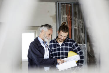Architect explaining building plan to worker on a construction site - MJFKF00238