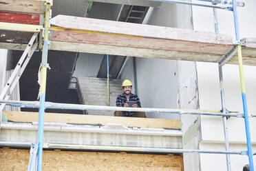 Lächelnder Arbeiter mit Tablet auf einer Baustelle - MJFKF00245