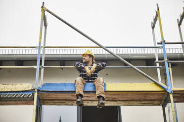 Arbeiter macht eine Pause auf einem Baugerüst auf einer Baustelle - MJFKF00247