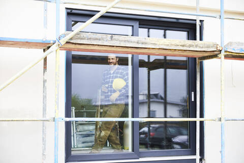 Arbeiter hinter einem Fenster auf einer Baustelle stehend, lizenzfreies Stockfoto