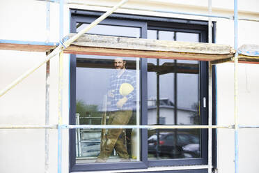 Arbeiter hinter einem Fenster auf einer Baustelle stehend - MJFKF00251