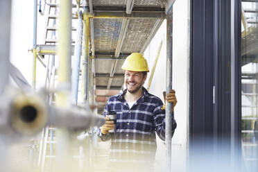 Happy worker having a coffee break on a construction site - MJFKF00257