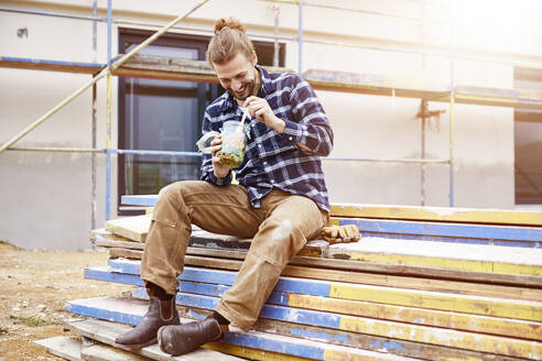 Happy worker having lunch break on a construction site - MJFKF00261