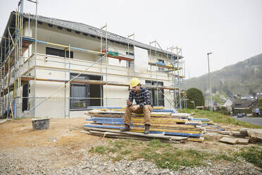 Arbeiter auf einer Baustelle, der eine Pause macht und sein Mobiltelefon überprüft - MJFKF00264