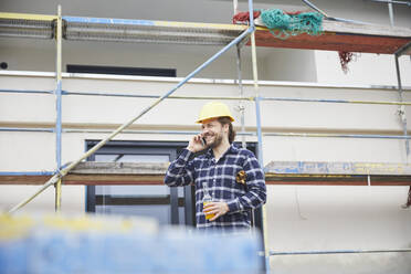 Smiling worker on the phone a construction site - MJFKF00265