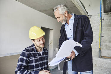 Architect and worker discussing building plan on a construction site - MJFKF00271