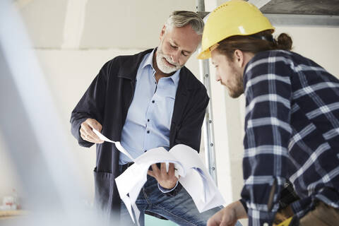 Architekt und Arbeiter besprechen einen Bauplan auf einer Baustelle, lizenzfreies Stockfoto