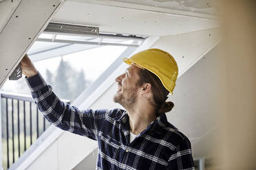 Smiling worker at the window on a construction site - MJFKF00278