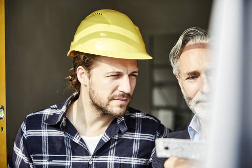 Architekt und Arbeiter messen Fenster auf einer Baustelle aus - MJFKF00280