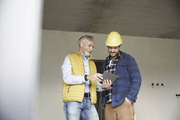 Architekt und Arbeiter teilen sich ein Tablet auf einer Baustelle - MJFKF00287