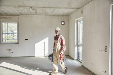 Construction worker with drill and tool box at construction site - MJFKF00293