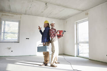 Smiling construction workers with drill and tool box at construction site - MJFKF00298