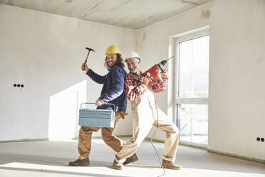 Smiling construction workers with drill and tool box at construction site - MJFKF00299