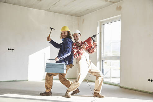 Lächelnde Bauarbeiter mit Bohrmaschine und Werkzeugkasten auf der Baustelle - MJFKF00299
