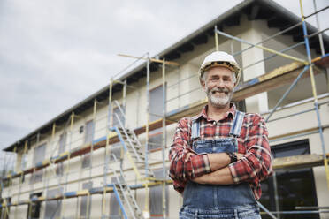 Smiling construction worker with crossed arms at construction site - MJFKF00311