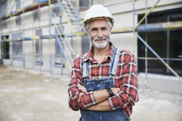 Smiling construction worker with crossed arms at construction site - MJFKF00312